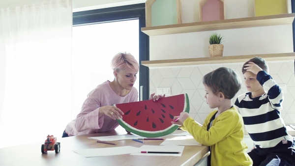 A happy young woman with two children drawing pictures in a kitchen. Slow motion.