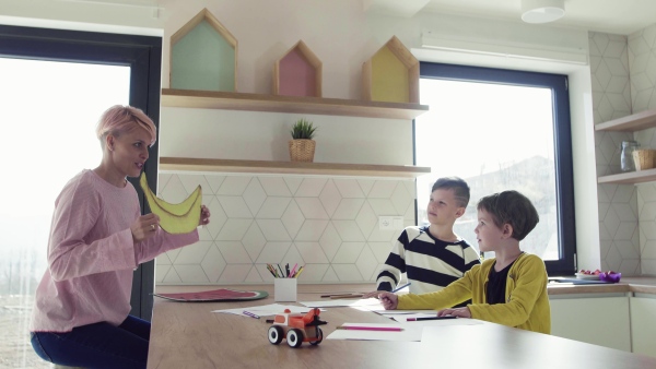 A happy young woman with two children drawing pictures in a kitchen.