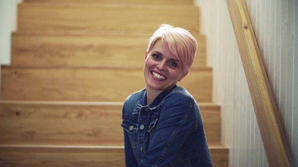 A young attractive woman sitting at the bottom of the stairs at home, laughing. Slow motion.