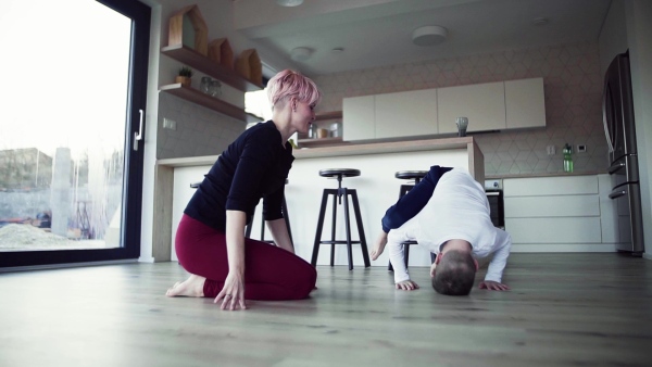 A young mother doing exercise with small son indoors at home. Slow motion.