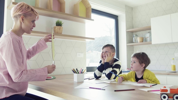 A happy young woman with two children drawing pictures in a kitchen.