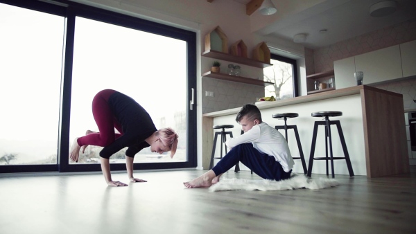 A young mother doing exercise with small son indoors at home. Slow motion.