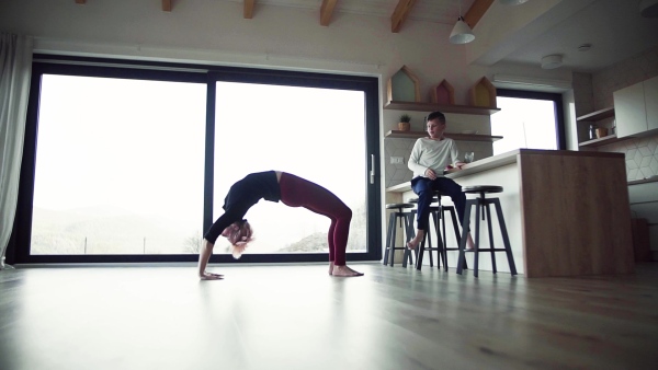 A young mother doing bridge exercise with small son indoors at home. Slow motion.