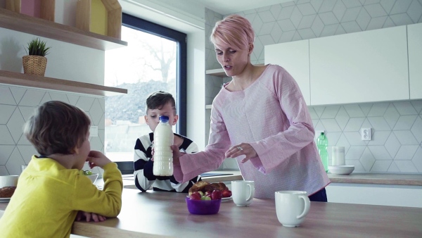 A young mother with two happy children having snack in a kitchen. Slow motion.