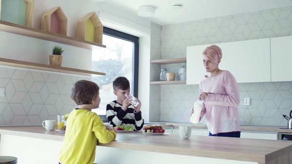 A young mother with two happy children having snack in a kitchen. Slow motion.