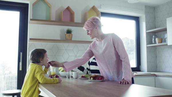 A young mother with two happy children eating fruit in a kitchen. Slow motion.