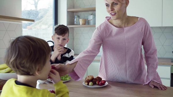 A young mother with two happy children eating fruit in a kitchen. Slow motion.