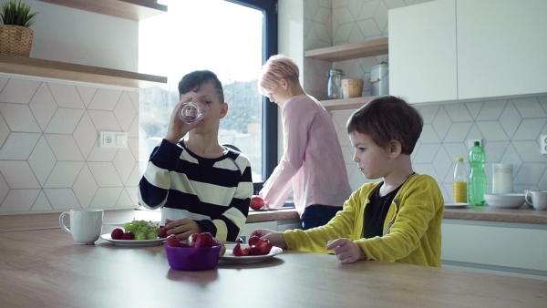 A young mother with two happy children eating fruit in a kitchen. Slow motion.