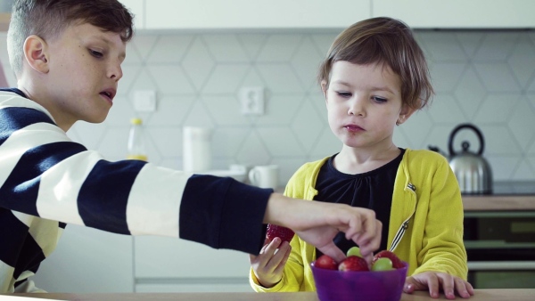 A young mother with two happy children eating fruit in a kitchen. Slow motion.