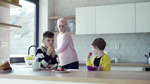 A young mother with two happy children eating fruit in a kitchen. Slow motion.