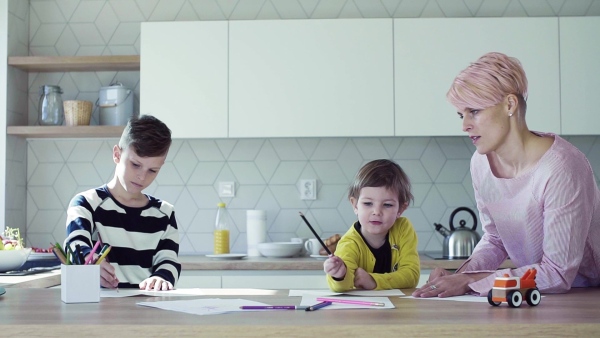 A happy young mother with two children drawing pictures in a kitchen. Slow motion.