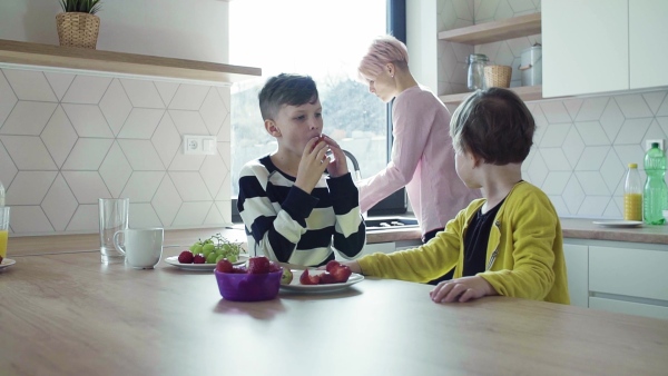 A young mother with two happy children eating fruit in a kitchen. Slow motion.