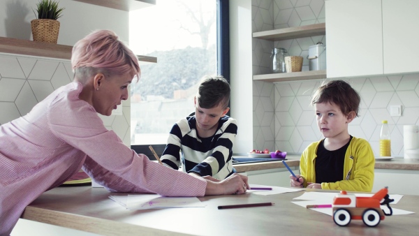 A happy young mother with two children drawing pictures in a kitchen.