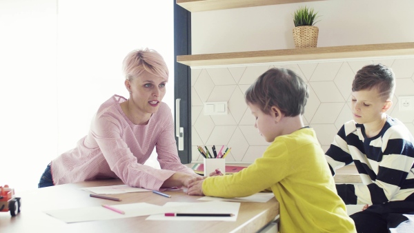 A happy young woman with two children drawing pictures in a kitchen.