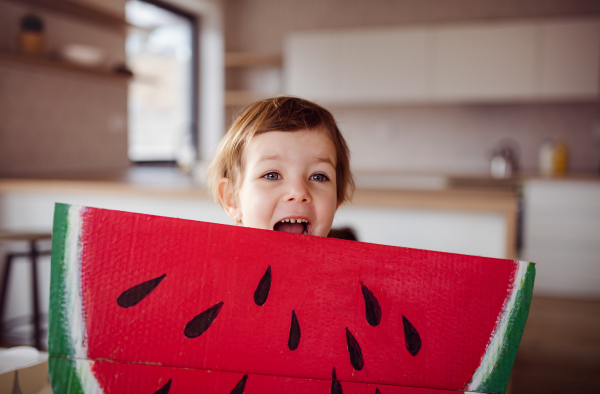 A small girl with large paper watermelon toy fruit at home, eating fruit concept.