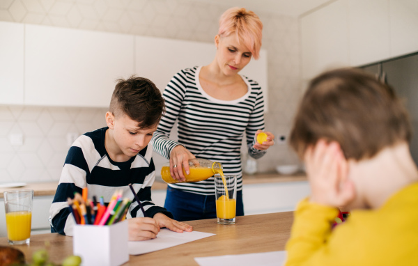 A young woman with two happy children drawing in a kitchen.