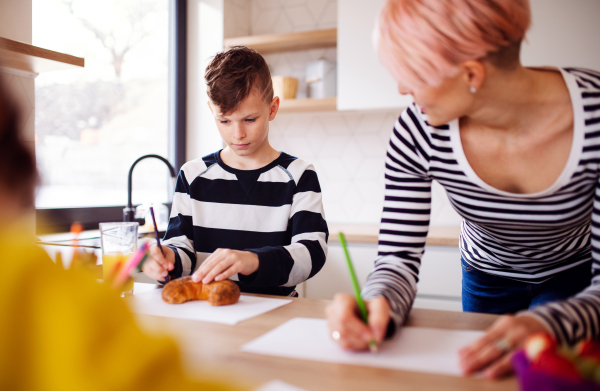 A young woman with two happy children drawing in a kitchen.