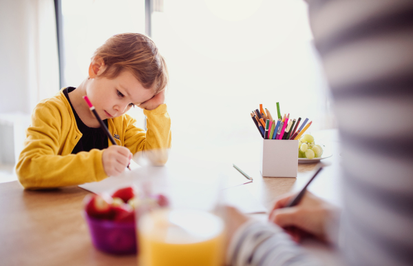 An unrecognizable mother with small daughter drawing pictures in a kitchen.