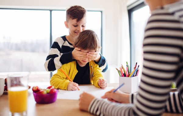 A young woman with two happy children drawing in a kitchen.