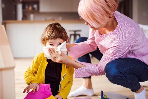 Young mother blowing her small daughter's nose when playing at home.