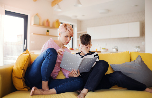 A young woman with a small son indoors at home, reading a book.