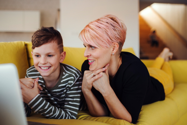 A young woman with a small son lying on a sofa at home, using laptop.