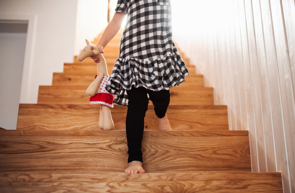 A midsection of unrecognizable small child with a soft toy walking down the stairs.