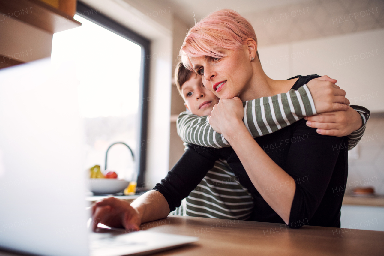 A young woman with a small son using laptop in a kitchen at home, working.