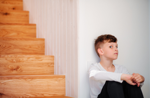 A small boy sitting on the floor by the stairs, grimacing. Copy space.