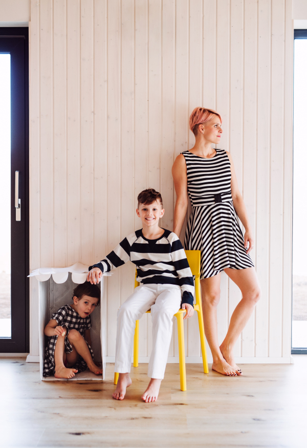 Young woman with two children in black and white clothes against white wooden wall.