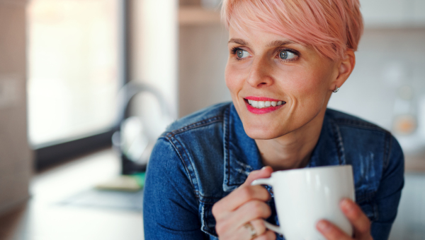 A young attractive woman with a coffee leaning on a counter in a kitchen at home.