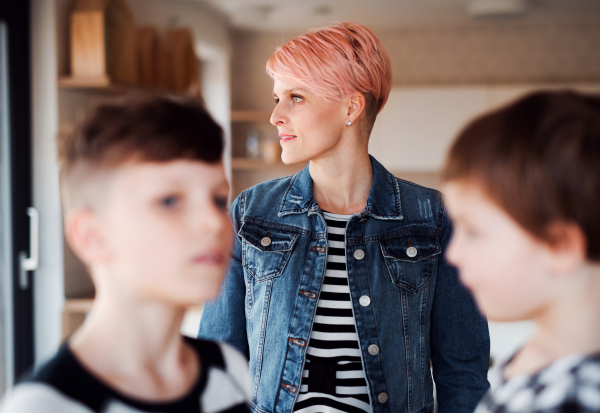 A young woman with two children standing at home, focus on background.