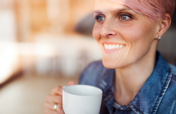 A close-up portrait of young attractive woman standing by window at home. Shot through glass.