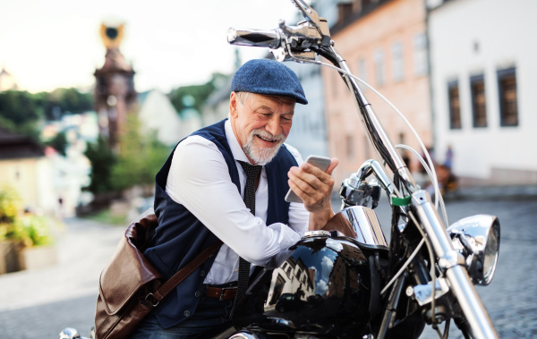 A cheerful senior businessman with motorbike in town, using smartphone.