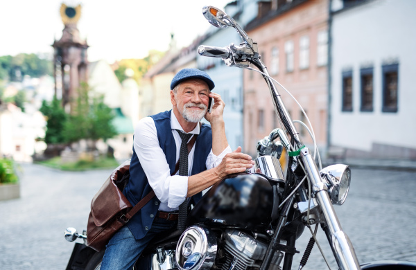 A cheerful senior businessman with motorbike in town, using smartphone.