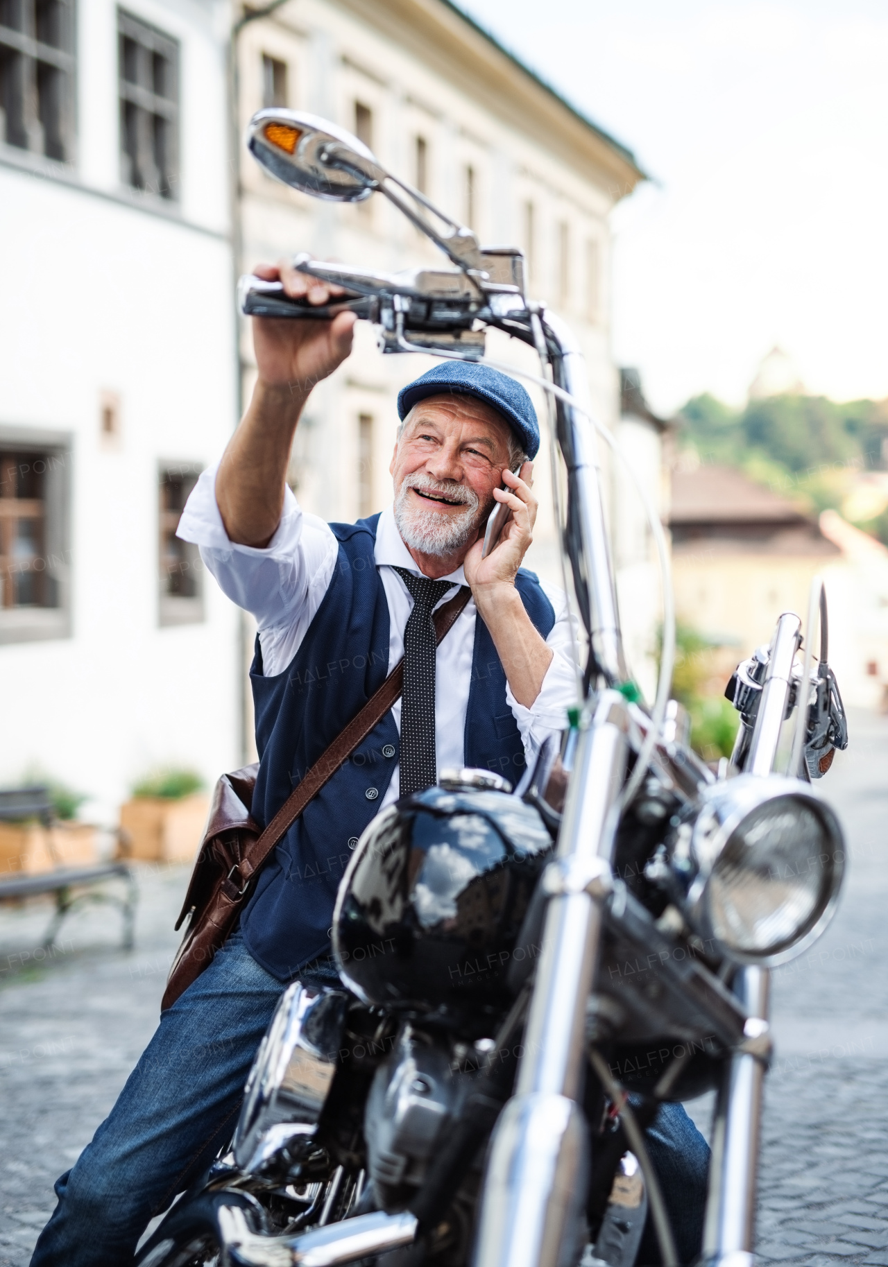 A cheerful senior businessman with motorbike in town, using smartphone.