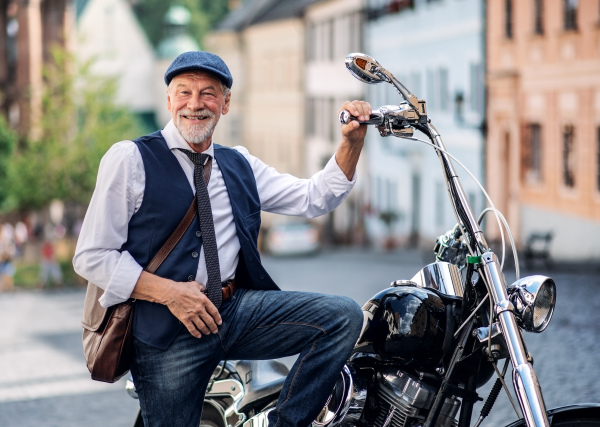 A happy senior businessman with motorbike in town.