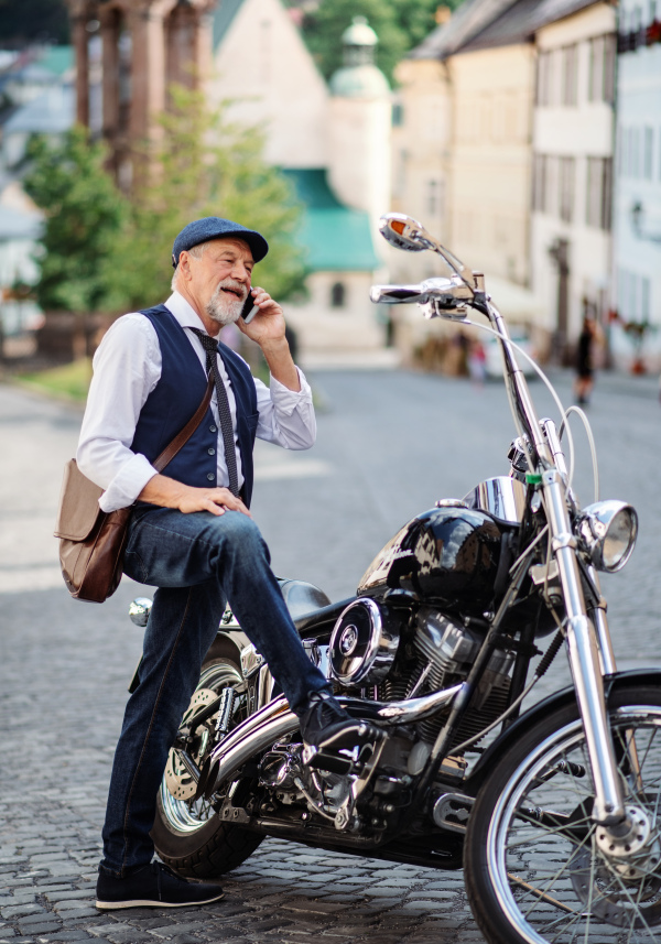 A cheerful senior businessman with motorbike in town, using smartphone.