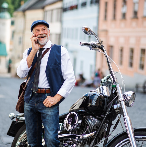 A cheerful senior businessman with motorbike in town, using smartphone.