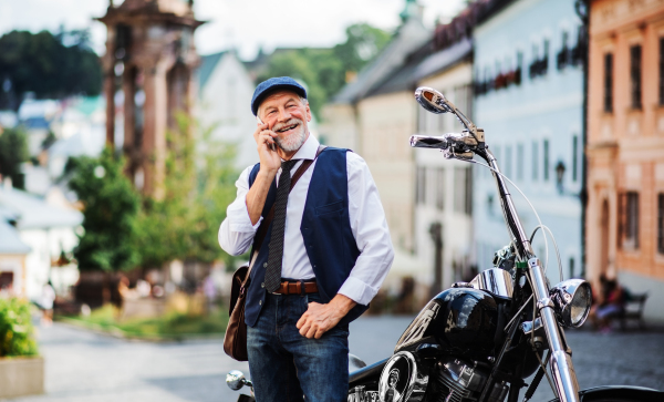 A cheerful senior businessman with motorbike in town, using smartphone.