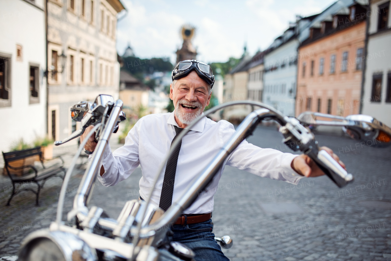 A cheerful senior businessman with motorbike in town, looking at camera.