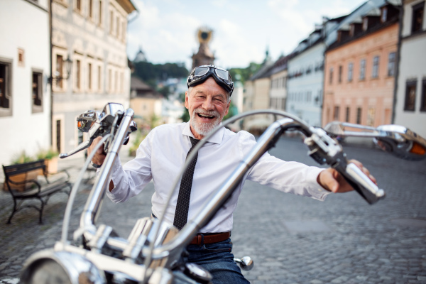 A cheerful senior businessman with motorbike in town, looking at camera.