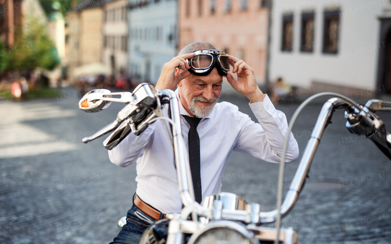 A cheerful senior businessman with motorbike in town, putting on goggles.