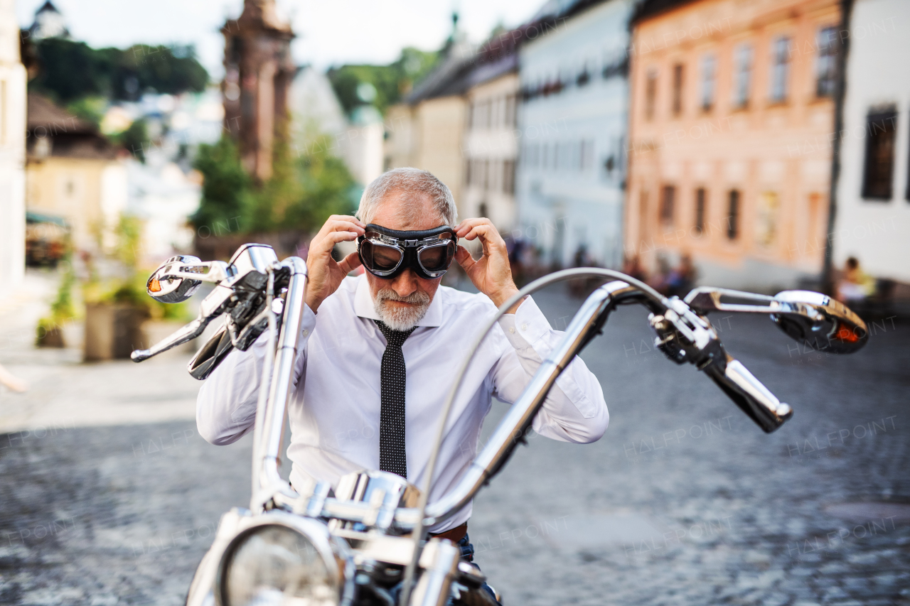 A cheerful senior businessman with motorbike in town, putting on goggles.