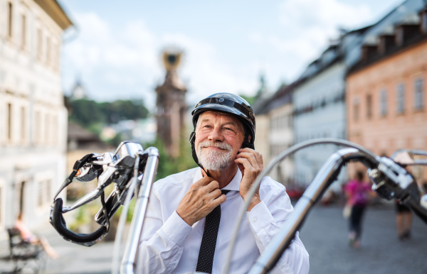 A cheeful senior businessman with motorbike in town, putting on helmet.