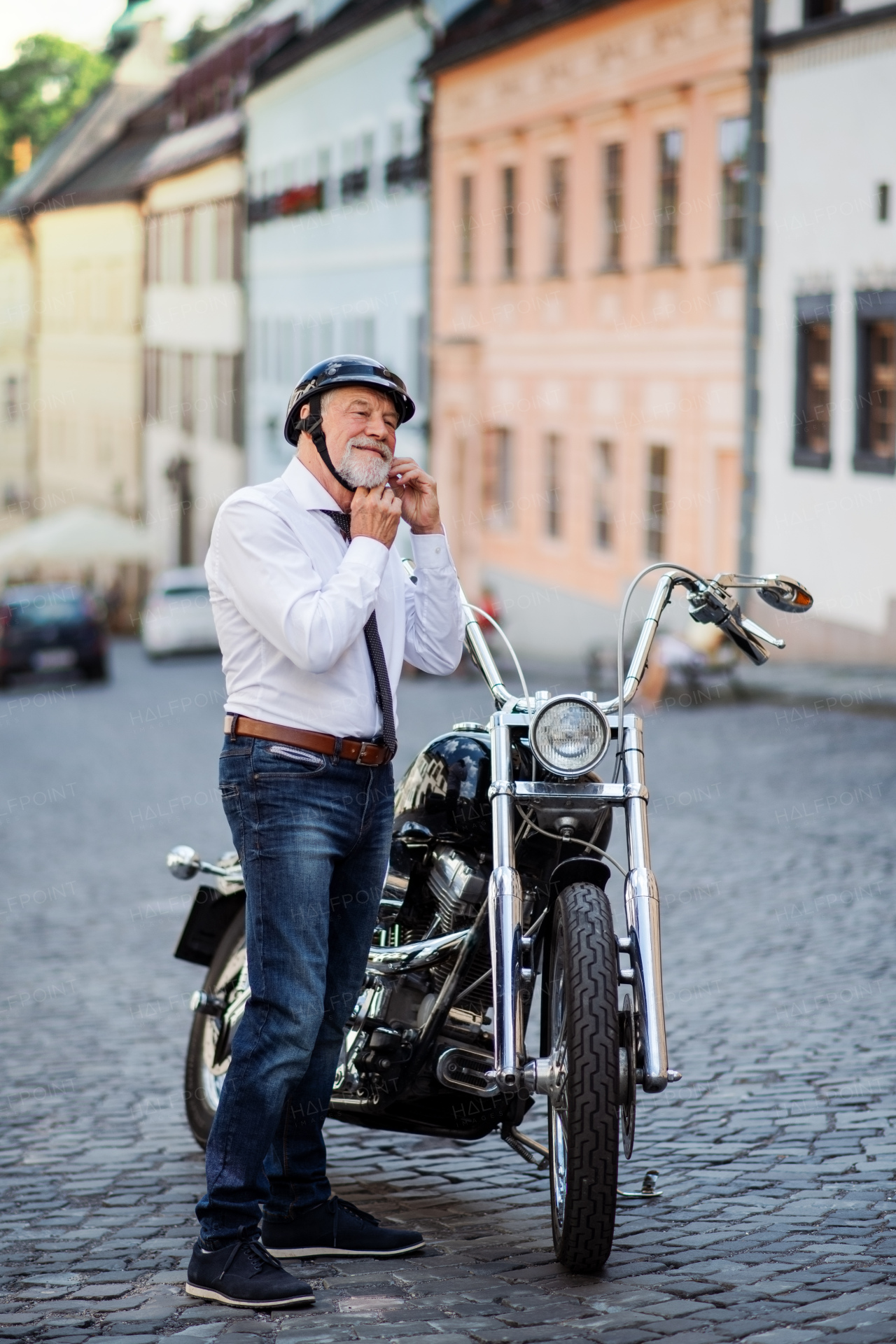 A cheeful senior businessman with motorbike in town, putting on helmet.