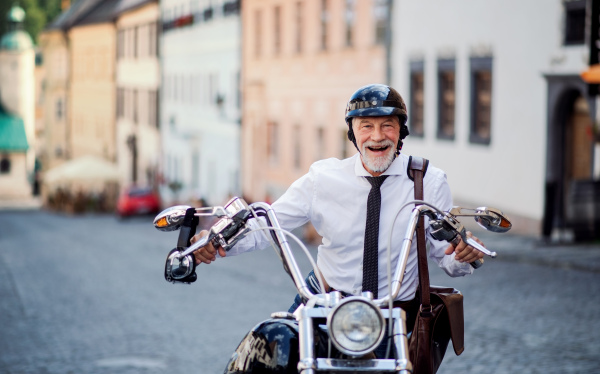 A cheerful senior businessman with motorbike in town, looking at camera.