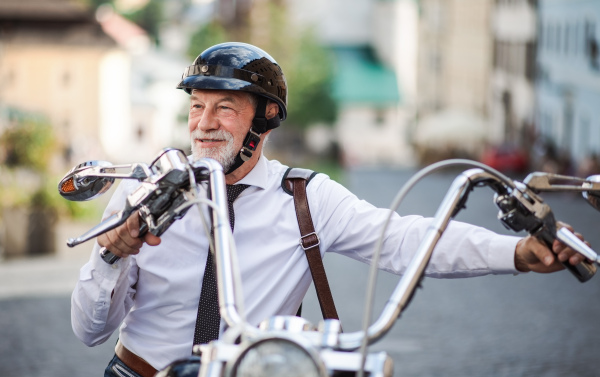 A front view of senior businessman with motorbike in town.