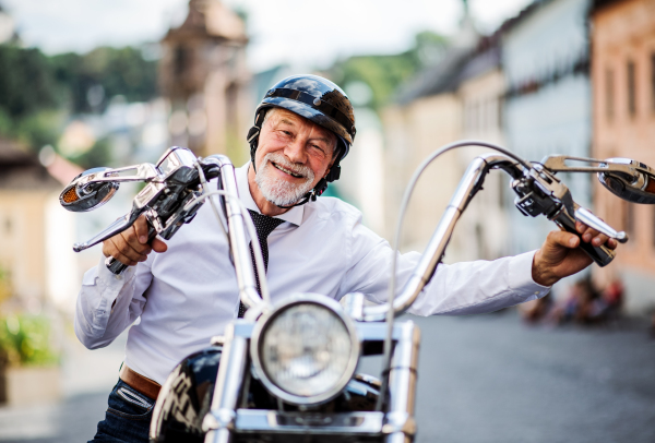 A cheerful senior businessman with motorbike in town, looking at camera.