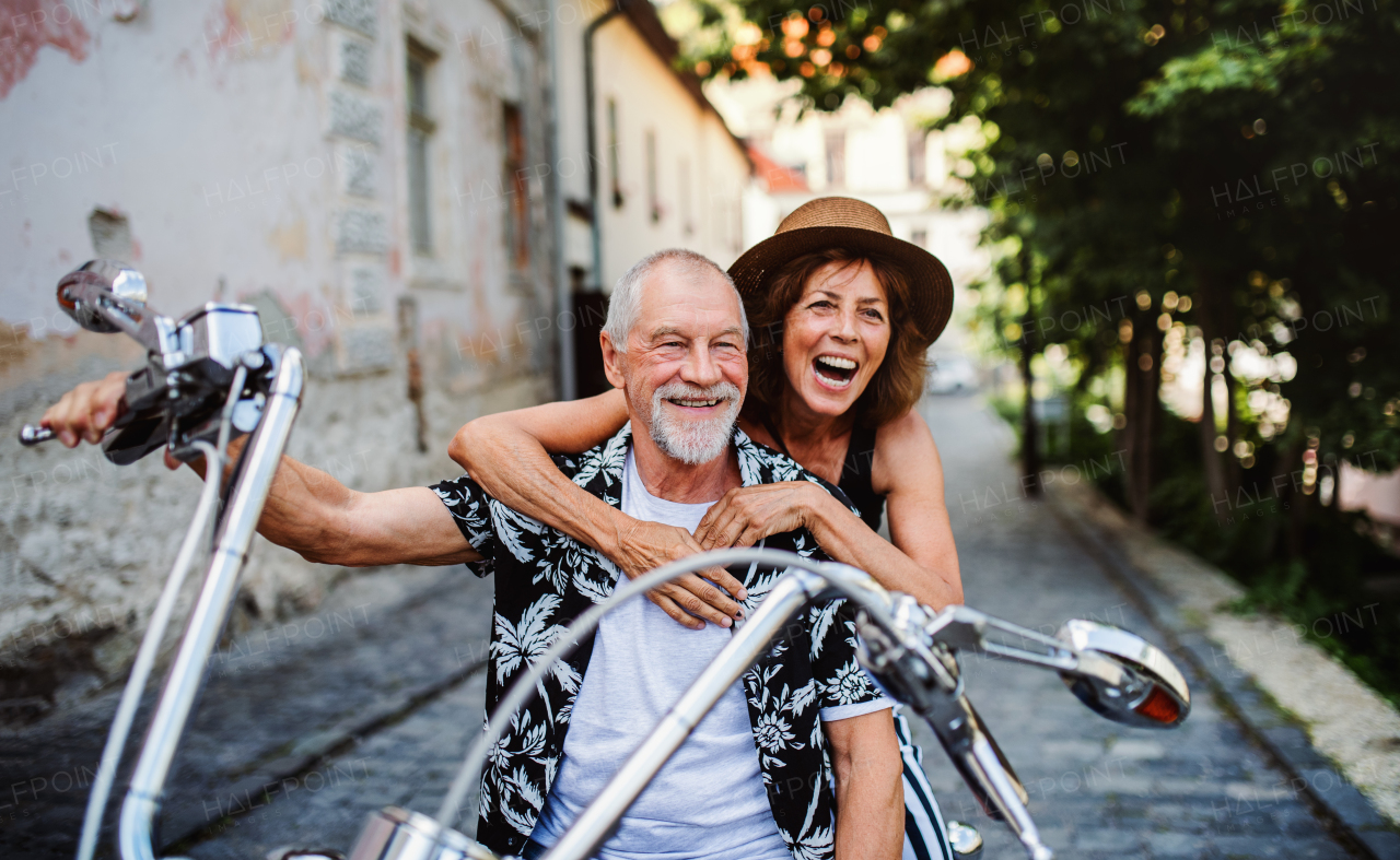 A front view of cheerful senior couple travellers with motorbike in town.